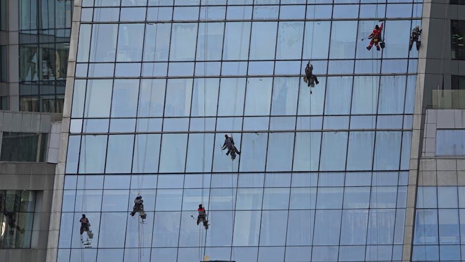 Workers using ropes to clean large glass building facade, showcasing urban maintenance.