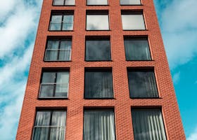 Red-brick modern building against a vibrant blue sky and clouds.
